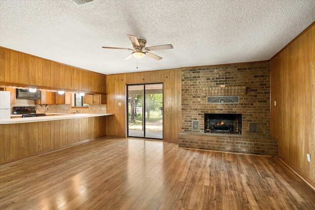 1023 Holmes Dr, Granbury, TX 76048 - kitchen with black appliances, brown cabinets, wooden walls, a ceiling fan, and open floor plan