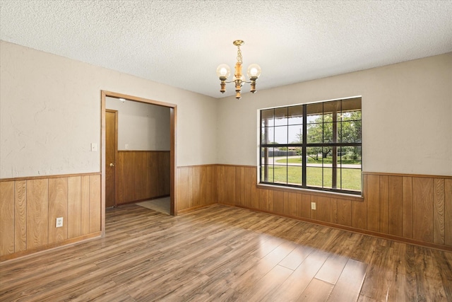 1023 Holmes Dr, Granbury, TX 76048 - empty room featuring wood finished floors, a chandelier, wainscoting, a textured ceiling, and wooden walls