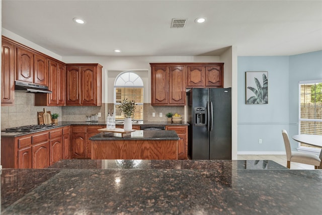 8620 Thistle Ridge Ter, Fort Worth, TX 76123 - kitchen featuring black fridge with ice dispenser, stainless steel gas cooktop, under cabinet range hood, dark stone counters, and tasteful backsplash