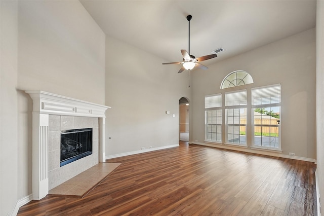 2110 Pecan Ridge Dr, Forney, TX 75126 - unfurnished living room featuring wood finished floors, a ceiling fan, a fireplace, arched walkways, and a high ceiling
