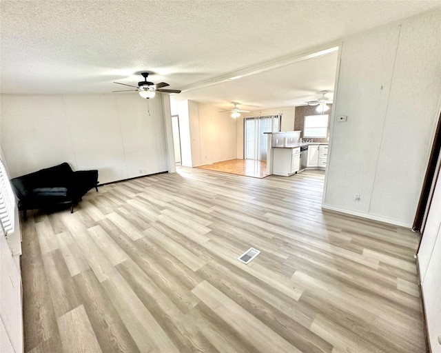 6818 Spring Shower Ct, Krum, TX 76249 - unfurnished living room featuring light wood-style flooring, ceiling fan, and a textured ceiling