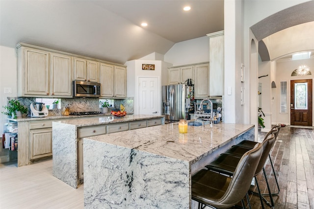 6004 Grand Meadow Ln, Flower Mound, TX 75028 - kitchen featuring stainless steel appliances, lofted ceiling, an island with sink, arched walkways, and light wood-type flooring