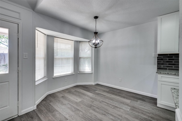 7708 Partridge Dr, Watauga, TX 76148 - unfurnished dining area with a chandelier, wood finished floors, a textured ceiling, and baseboards