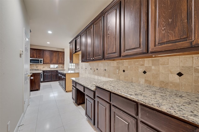 9122 Bottlebrush Ln, Irving, TX 75063 - kitchen featuring stainless steel microwave, decorative backsplash, dark brown cabinetry, light stone countertops, and recessed lighting