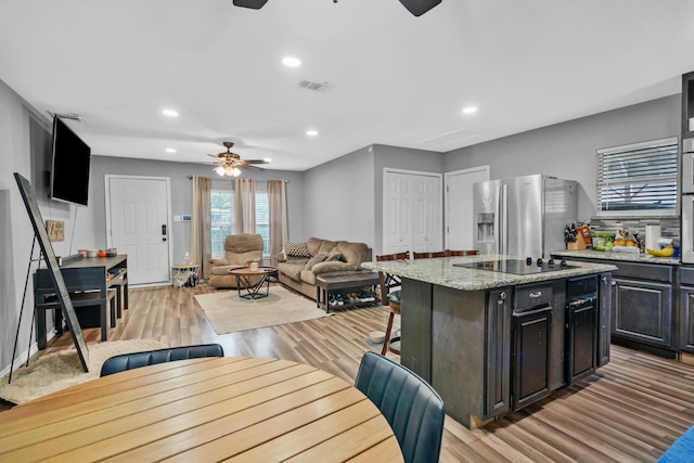 5340 Bourquin St, Dallas, TX 75210 - kitchen with a ceiling fan, stainless steel refrigerator with ice dispenser, black electric cooktop, a center island, and a kitchen bar