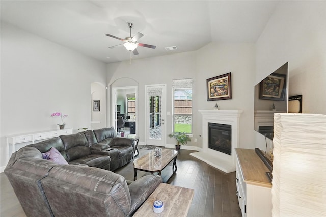 7817 Fossil Creek Trl, Mckinney, TX 75071 - living room with ceiling fan, dark wood-style flooring, a glass covered fireplace, arched walkways, and baseboards