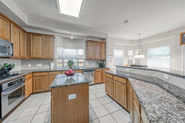 7908 Peacock Ln, Frisco, TX 75035 - kitchen with stainless steel appliances, a kitchen island, brown cabinets, tasteful backsplash, and dark stone countertops