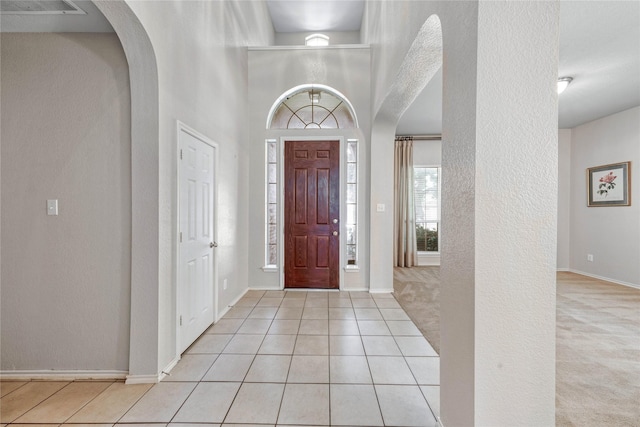 7908 Peacock Ln, Frisco, TX 75035 - carpeted foyer entrance featuring arched walkways, tile patterned floors, a textured wall, baseboards, and a high ceiling