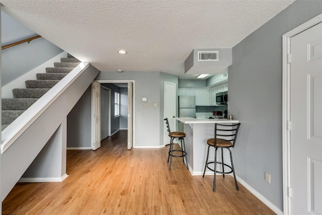 9815 Walnut St Unit 204, Dallas, TX 75243 - kitchen with stainless steel appliances, light wood-style floors, a breakfast bar, light countertops, and baseboards