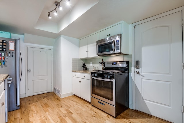 3964 Lost Creek Dr, Dallas, TX 75224 - kitchen with stainless steel appliances, light wood-style floors, decorative backsplash, white cabinets, and a tray ceiling