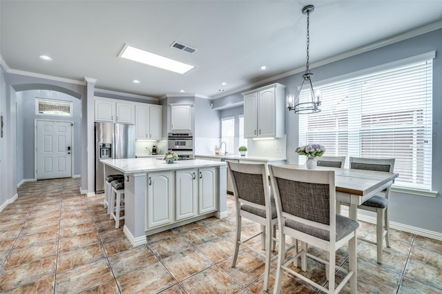 11543 Las Polamas Dr, Frisco, TX 75033 - kitchen featuring stainless steel appliances, crown molding, white cabinetry, light countertops, and a center island