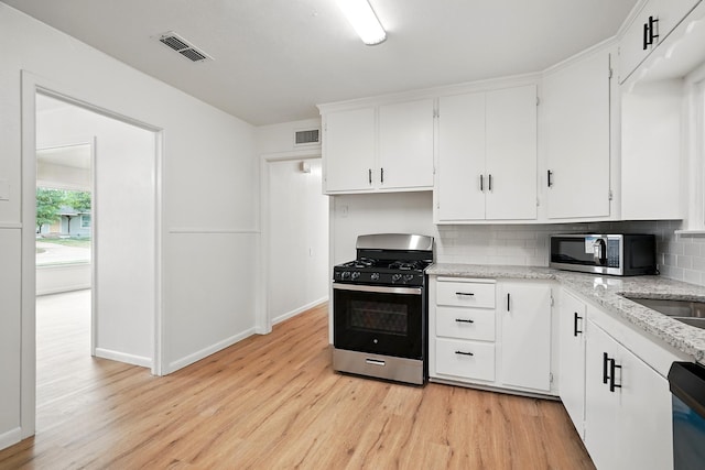 1942 Woodard St, Abilene, TX 79605 - kitchen with appliances with stainless steel finishes, light wood-style flooring, decorative backsplash, and white cabinetry