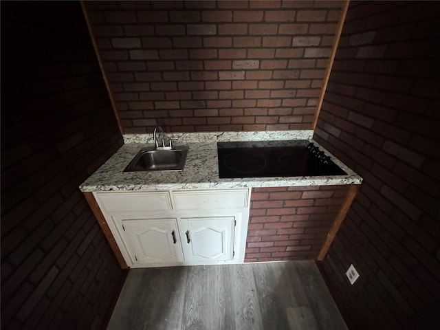 4312 Wheeler St, Bellmead, TX 76705 - kitchen with a sink, black electric cooktop, dark wood-type flooring, white cabinetry, and brick wall