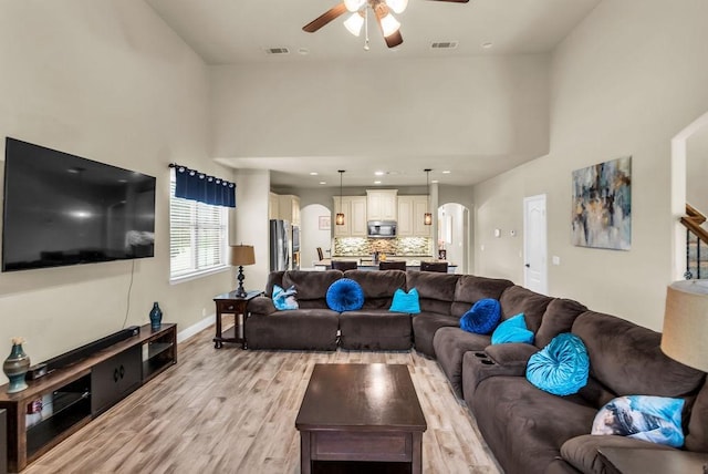 4323 Cherry Ln, Melissa, TX 75454 - living area featuring a ceiling fan, arched walkways, light wood-type flooring, a towering ceiling, and baseboards