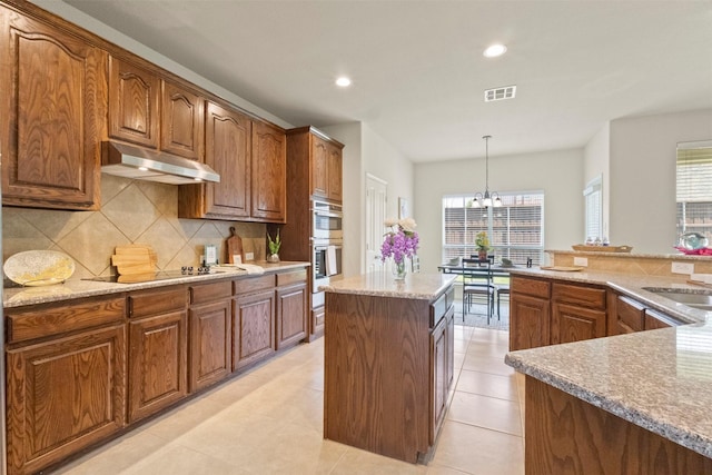 1713 Westfield Way, Allen, TX 75002 - kitchen with under cabinet range hood, black electric cooktop, a chandelier, backsplash, and stainless steel double oven