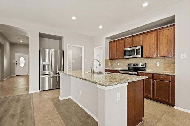 2004 Uvalde Dr, Forney, TX 75126 - kitchen with stainless steel appliances, arched walkways, backsplash, a center island with sink, and light tile patterned floors