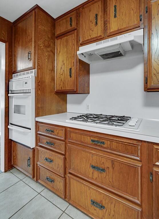 3732 N 24th St, Waco, TX 76708 - kitchen with a warming drawer, white appliances, brown cabinets, under cabinet range hood, and light tile patterned flooring