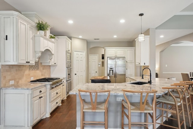 1300 Millers Creek Dr, Prosper, TX 75078 - kitchen featuring appliances with stainless steel finishes, arched walkways, a sink, dark wood-type flooring, and light stone countertops