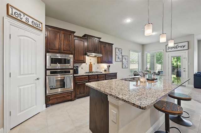 528 England St, Fate, TX 75189 - kitchen with appliances with stainless steel finishes, a sink, under cabinet range hood, light stone countertops, and a breakfast bar area