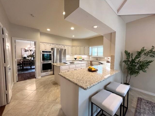 7009 Chevy Chase Ave, Dallas, TX 75225 - kitchen with appliances with stainless steel finishes, a peninsula, recessed lighting, light stone countertops, and a kitchen breakfast bar