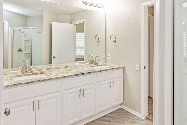 114 Juniper Dr, Arlington, TX 76018 - bathroom with wood finished floors, a stall shower, double vanity, a textured wall, and baseboards