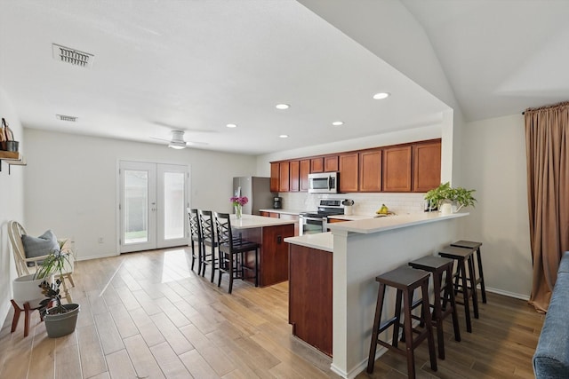 216 Hilltop Dr, Justin, TX 76247 - kitchen with appliances with stainless steel finishes, a kitchen breakfast bar, light countertops, light wood finished floors, and backsplash