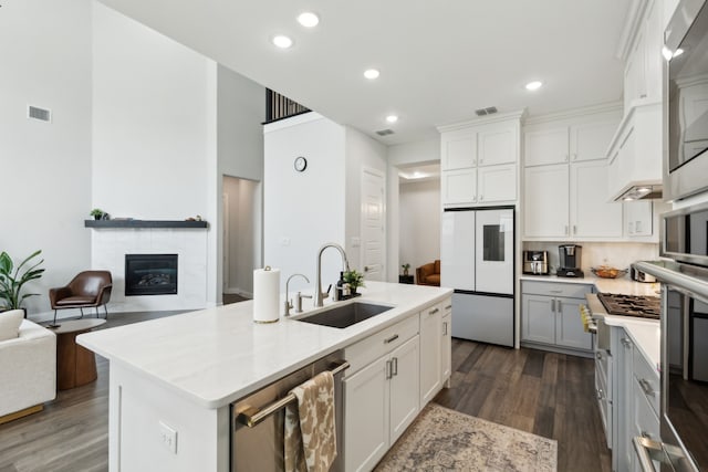 12469 Diamond Creek Dr, Frisco, TX 75035 - kitchen featuring appliances with stainless steel finishes, a sink, dark wood-type flooring, a tiled fireplace, and a kitchen island with sink