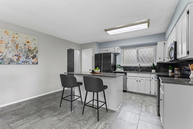 4910 Crest Dr, Arlington, TX 76017 - kitchen featuring stainless steel appliances, a kitchen island, a kitchen bar, white cabinets, and backsplash