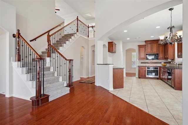 9004 Mcfarland Way, Fort Worth, TX 76244 - kitchen with black appliances, brown cabinets, arched walkways, a chandelier, and light wood-style floors