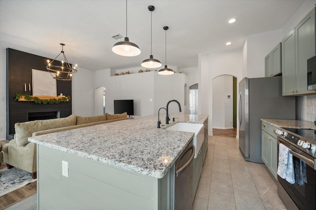 800 Bur Oak Dr, Burleson, TX 76028 - kitchen featuring arched walkways, appliances with stainless steel finishes, open floor plan, light stone counters, and a sink