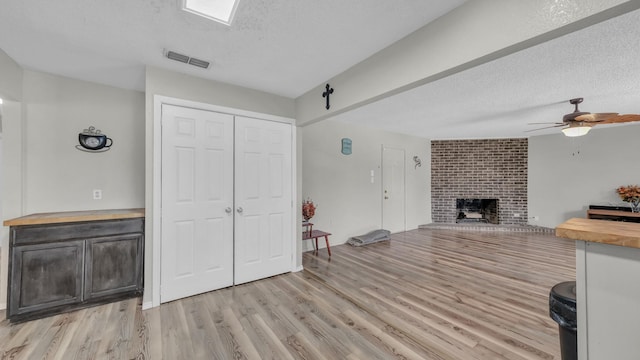 239 N 10th St, Jacksboro, TX 76458 - living room featuring a textured ceiling, light wood finished floors, a ceiling fan, and a fireplace