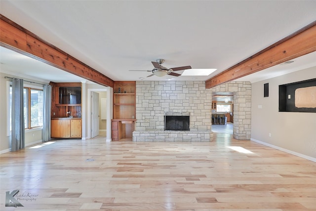 920 SW 3rd St, Hamlin, TX 79520 - unfurnished living room with ceiling fan, a stone fireplace, a skylight, baseboards, and beam ceiling