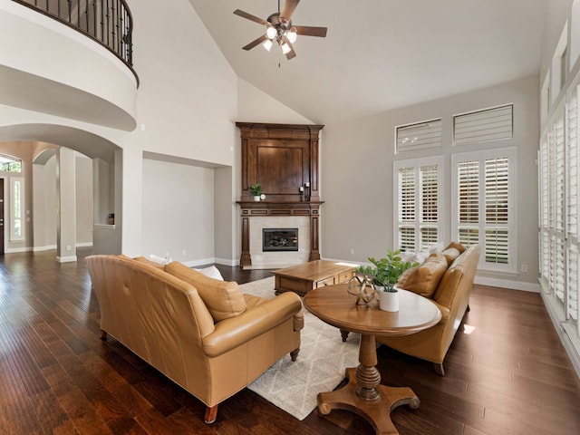 1025 Arches Park Dr, Allen, TX 75013 - living room featuring arched walkways, high vaulted ceiling, ceiling fan, a tiled fireplace, and dark wood-style flooring