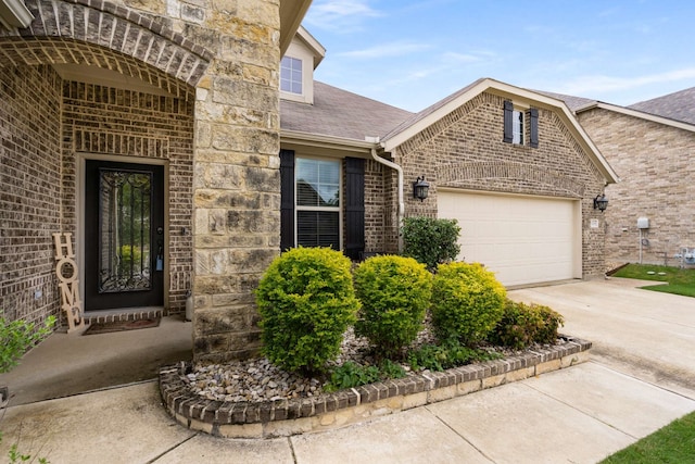 1129 Mesa Crest Dr, Fort Worth, TX 76052 - view of exterior entry featuring a garage, concrete driveway, brick siding, a shingled roof, and stone siding