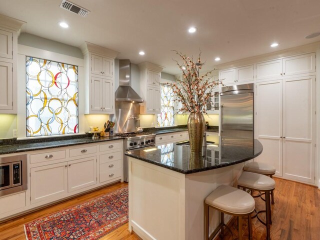 6319 Mccommas Blvd, Dallas, TX 75214 - kitchen featuring wall chimney range hood, built in appliances, light wood-style flooring, a kitchen breakfast bar, and a center island