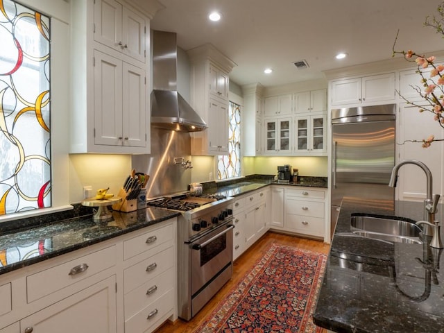 6319 Mccommas Blvd, Dallas, TX 75214 - kitchen featuring high end appliances, wall chimney range hood, a sink, light wood finished floors, and white cabinets