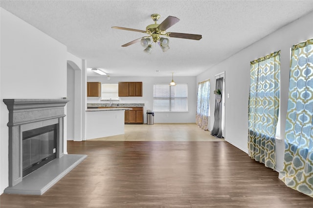 8300 Southern Prairie Dr, Fort Worth, TX 76123 - unfurnished living room featuring a textured ceiling, a sink, a ceiling fan, light wood-type flooring, and a glass covered fireplace