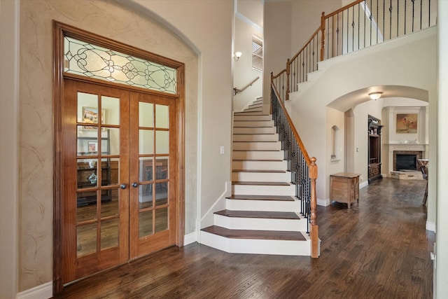 1205 Platte Dr, Mansfield, TX 76063 - staircase featuring french doors, a fireplace with raised hearth, wood finished floors, a towering ceiling, and arched walkways