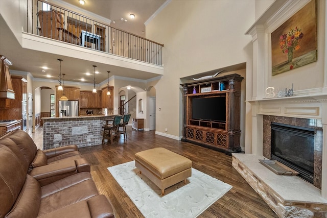 1205 Platte Dr, Mansfield, TX 76063 - living area with arched walkways, a high ceiling, a premium fireplace, ornamental molding, and dark wood-style floors