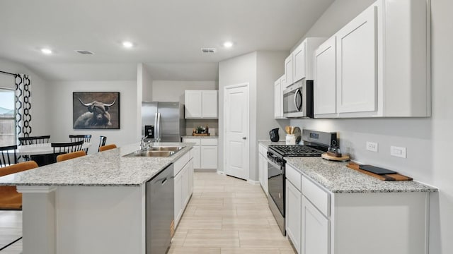 8417 Stout Dr, Fort Worth, TX 76131 - kitchen with appliances with stainless steel finishes, a breakfast bar area, a kitchen island with sink, white cabinetry, and recessed lighting