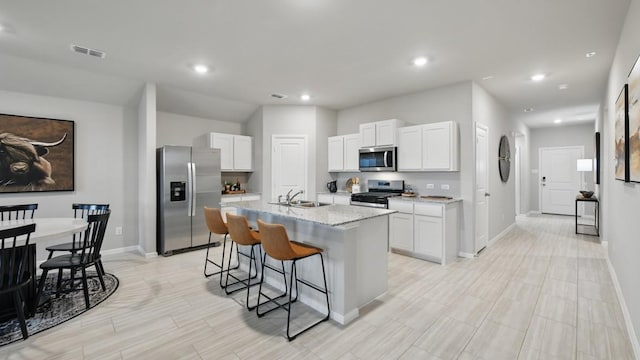 8417 Stout Dr, Fort Worth, TX 76131 - kitchen with appliances with stainless steel finishes, baseboards, a center island with sink, a kitchen bar, and white cabinetry