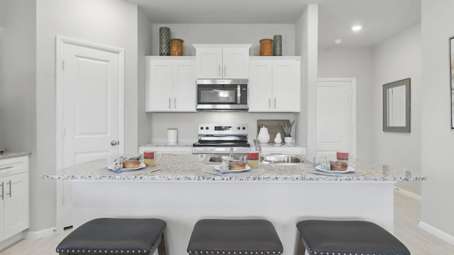 857 Cedarbrook, Fort Worth, TX 76131 - kitchen featuring appliances with stainless steel finishes, white cabinets, a center island with sink, a breakfast bar area, and baseboards