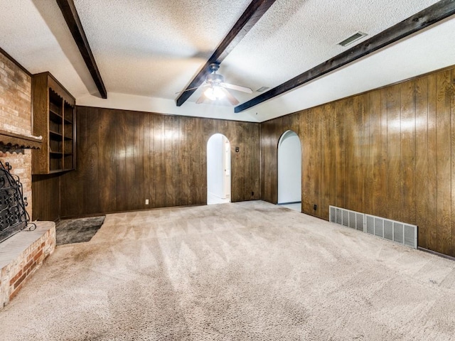 809 S Ridgeway Dr, Cleburne, TX 76033 - unfurnished living room featuring arched walkways, beam ceiling, wooden walls, a textured ceiling, and carpet