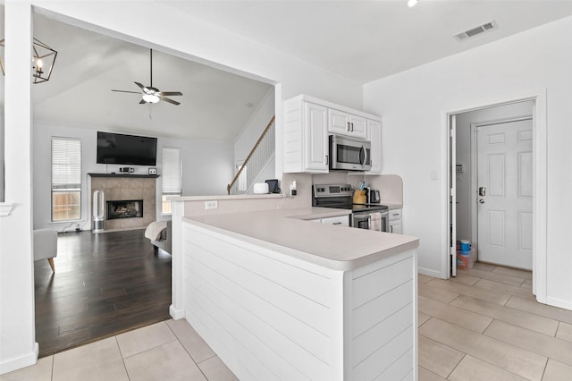 4100 Creekhollow Dr, Carrollton, TX 75010 - kitchen featuring appliances with stainless steel finishes, a peninsula, ceiling fan, light countertops, and a fireplace