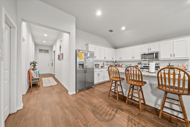 609 Autumn Ave, Justin, TX 76247 - kitchen with appliances with stainless steel finishes, wood finished floors, a breakfast bar, white cabinetry, and vaulted ceiling