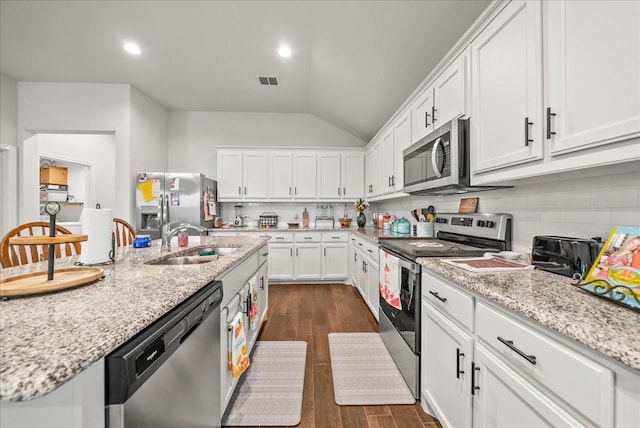 609 Autumn Ave, Justin, TX 76247 - kitchen with stainless steel appliances, a sink, vaulted ceiling, white cabinetry, and tasteful backsplash
