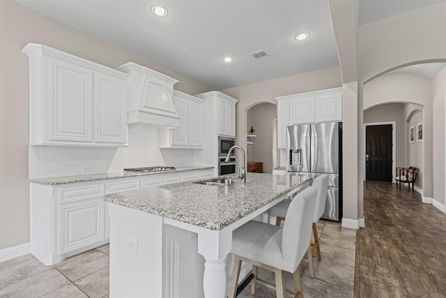 945 Colby Bluff Dr, Rockwall, TX 75087 - kitchen with arched walkways, appliances with stainless steel finishes, a sink, light stone counters, and a center island with sink