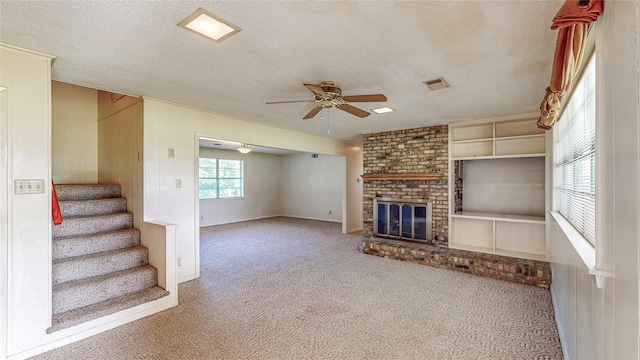 10335 Nolan Dr, Tyler, TX 75709 - unfurnished living room featuring carpet flooring, ceiling fan, a brick fireplace, a textured ceiling, and stairway