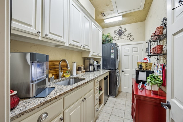 2590 King Arthur Blvd, Lewisville, TX 75056 - kitchen with stacked washer and clothes dryer, a sink, light tile patterned flooring, white cabinetry, and light stone countertops