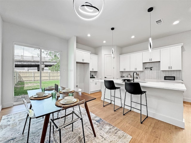 2419 Merlin St, Dallas, TX 75215 - kitchen featuring an island with sink, light wood-style floors, white cabinets, light countertops, and recessed lighting